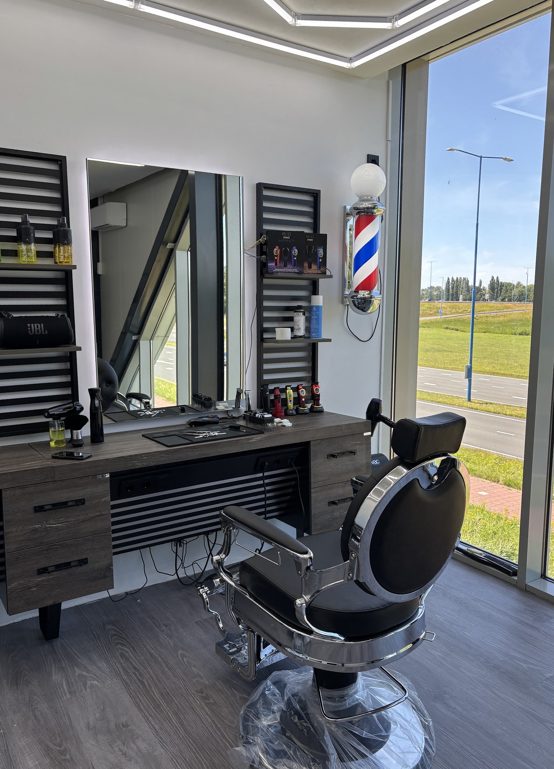 Een van de twee stations: zwarte barberstoel voor de spiegel, gestreepte barberpaal en het raam met uitzicht op het groen